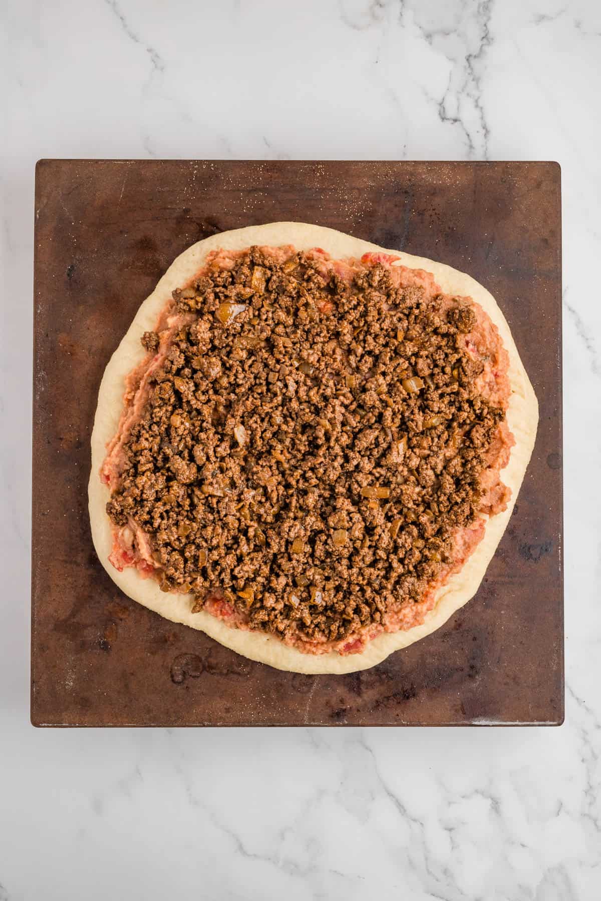 Adding a layer of ground beef taco meet to a taco pizza.