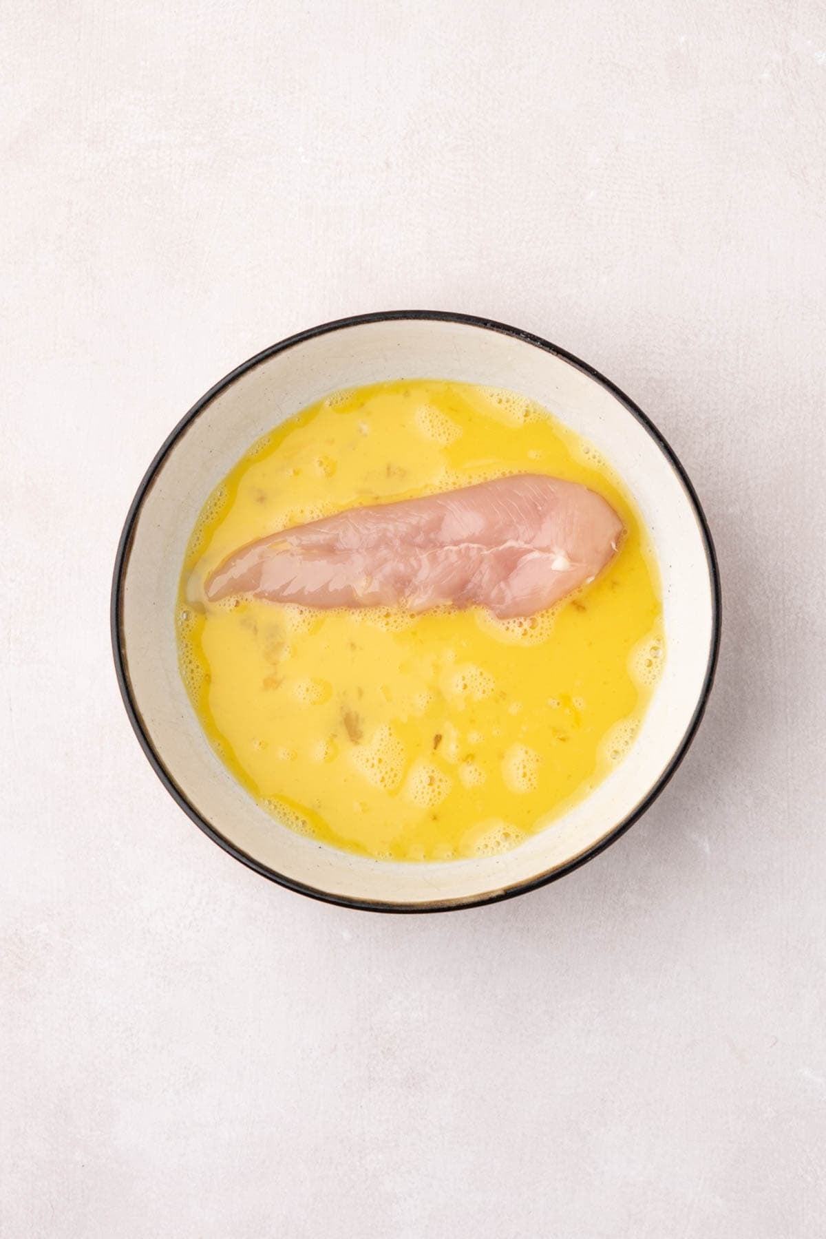 A chicken tender being dipped in beaten egg mixture.