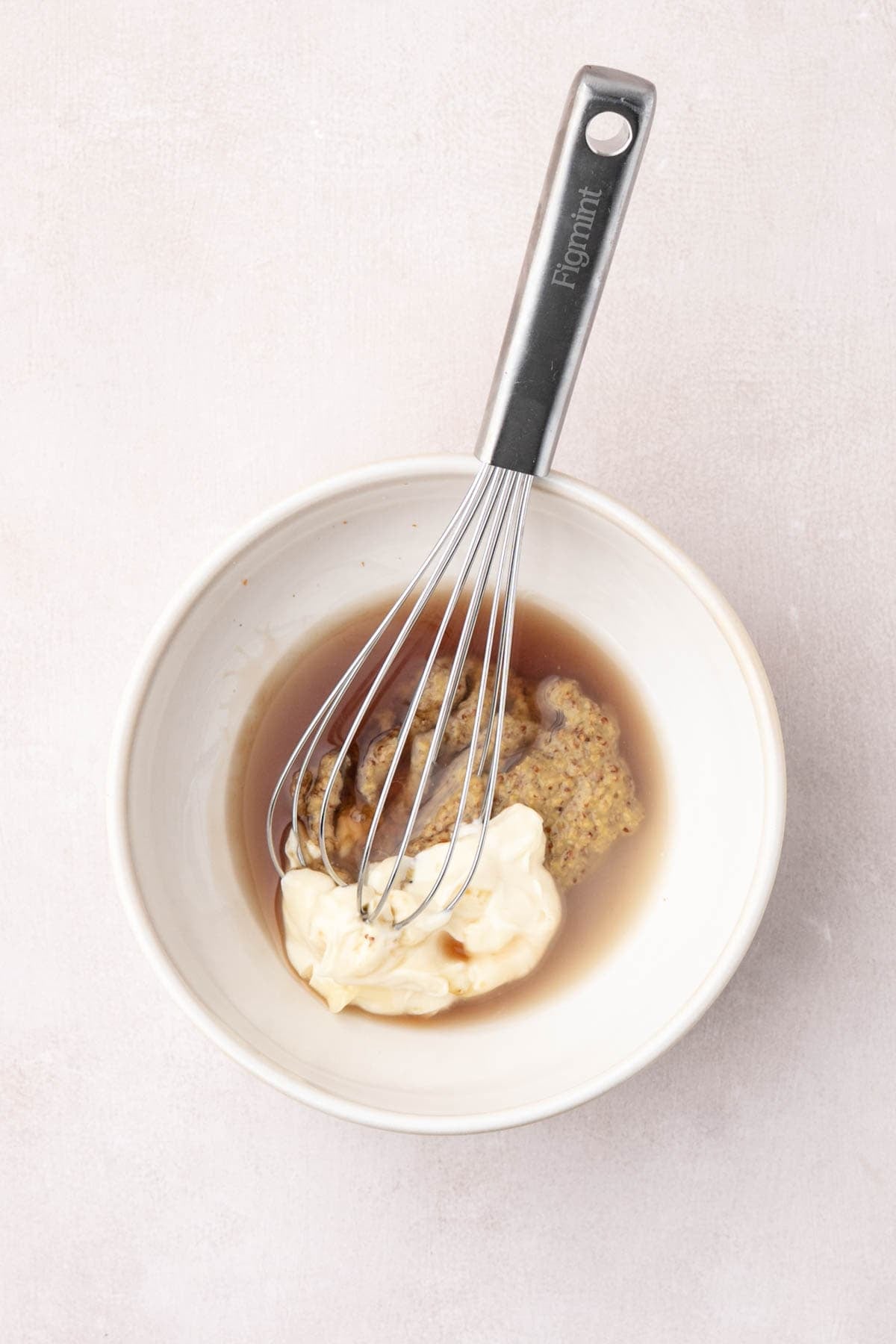 A whisk in a bowl of ingredients for honey mustard sauce.