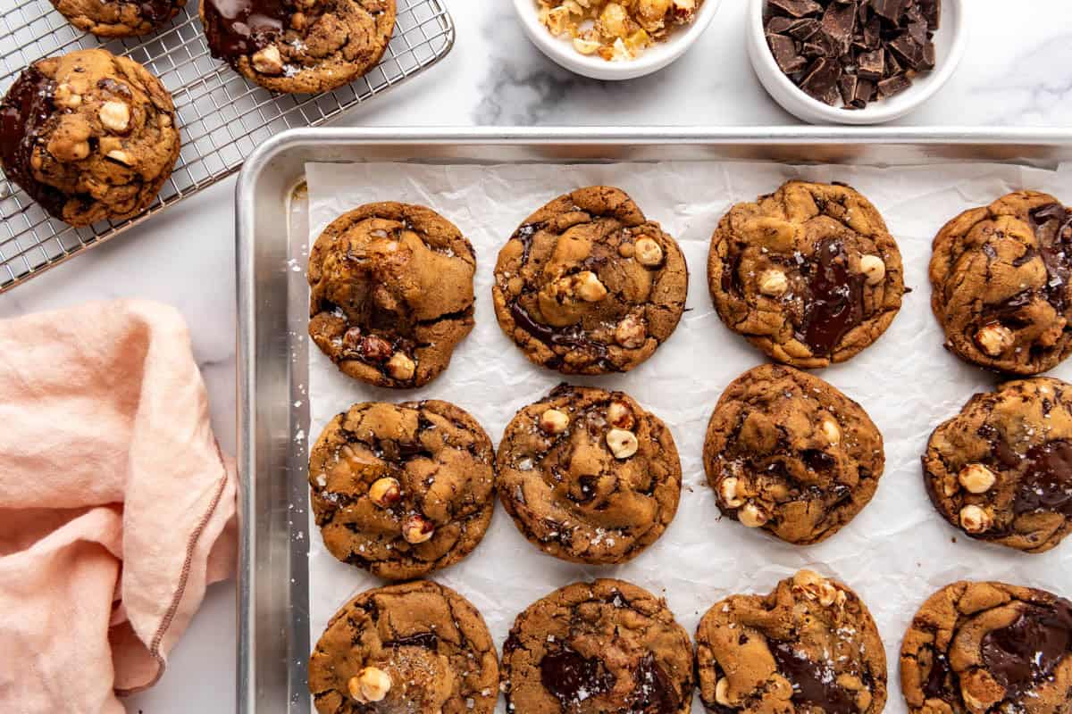 An overhead image of brown butter hazelnut chunk cookies on a baking sheet next to a pink cloth.