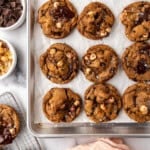 An overhead image of brown butter hazelnut chunk cookies on a baking sheet next to a pink cloth.