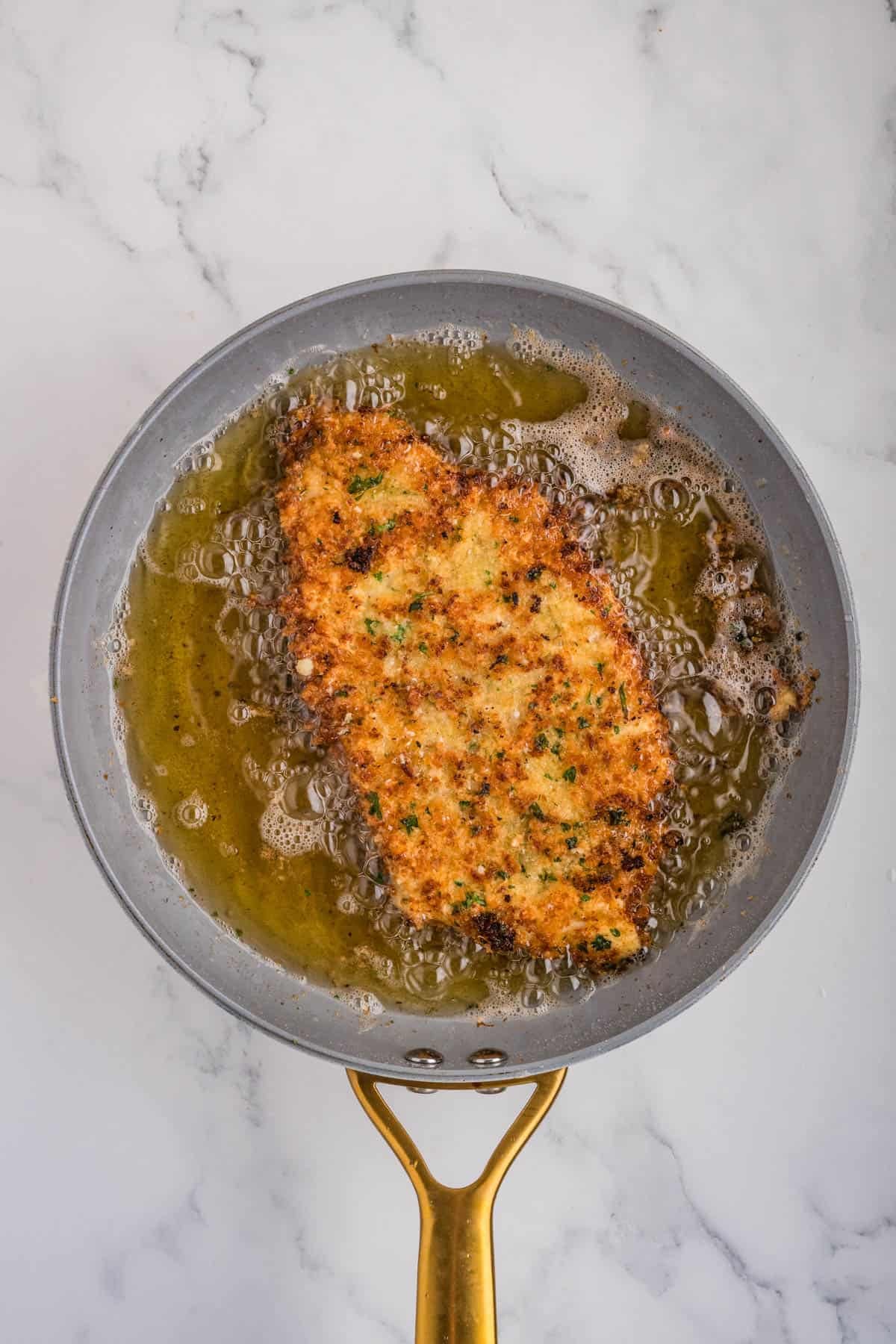 Golden brown chicken milanese in oil in a pan.