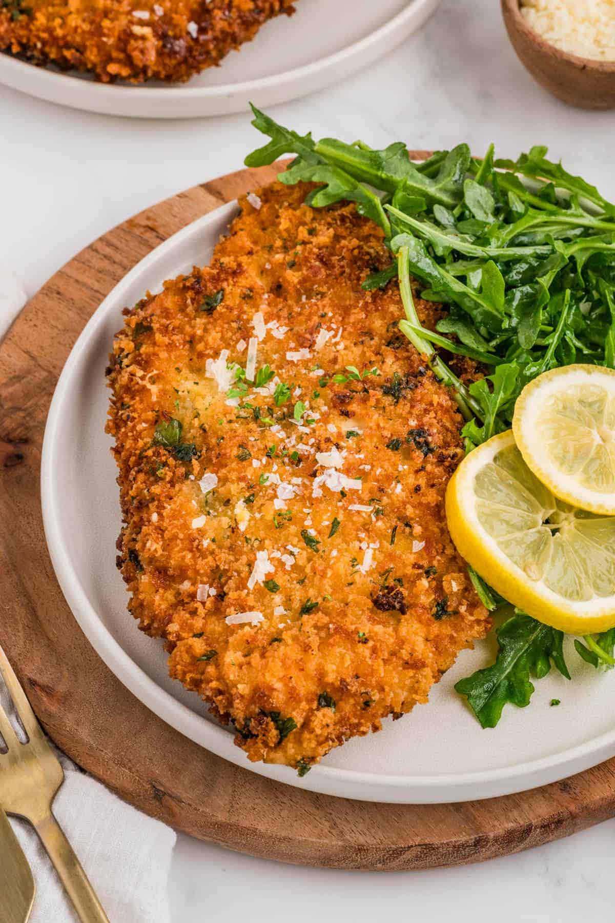 An image of chicken milanese on a plate with lemon slices and arugula.