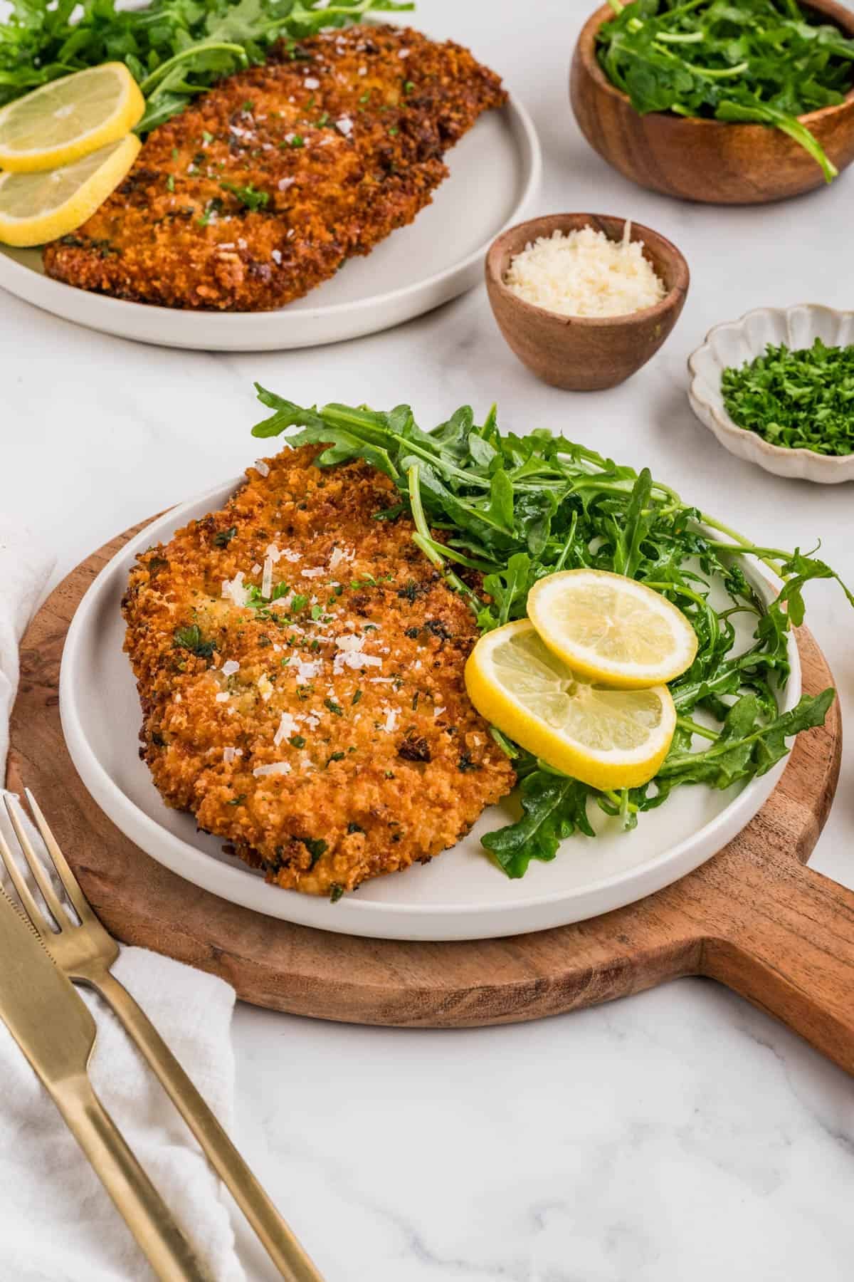 Plates of chicken milanese with lemon and arugula.