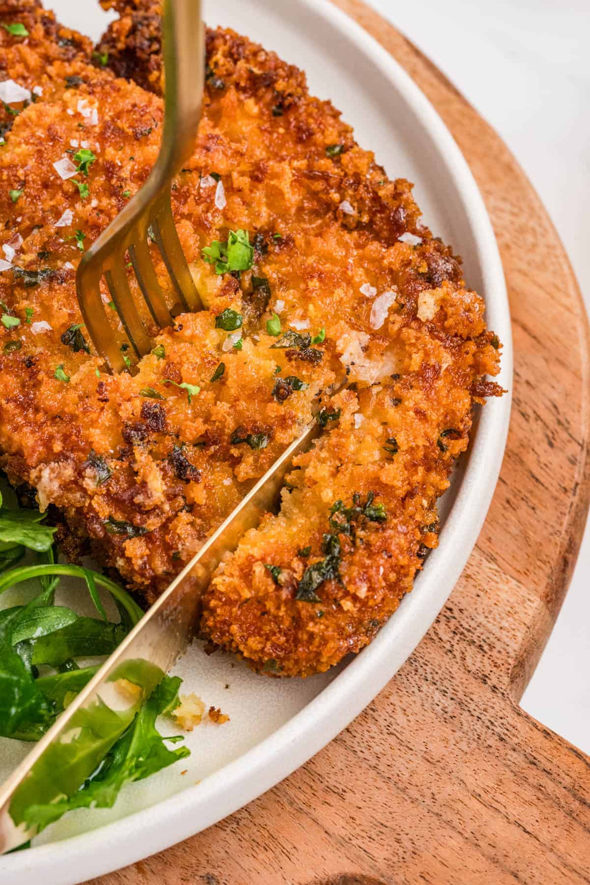 A knife and fork cutting into chicken milanese.