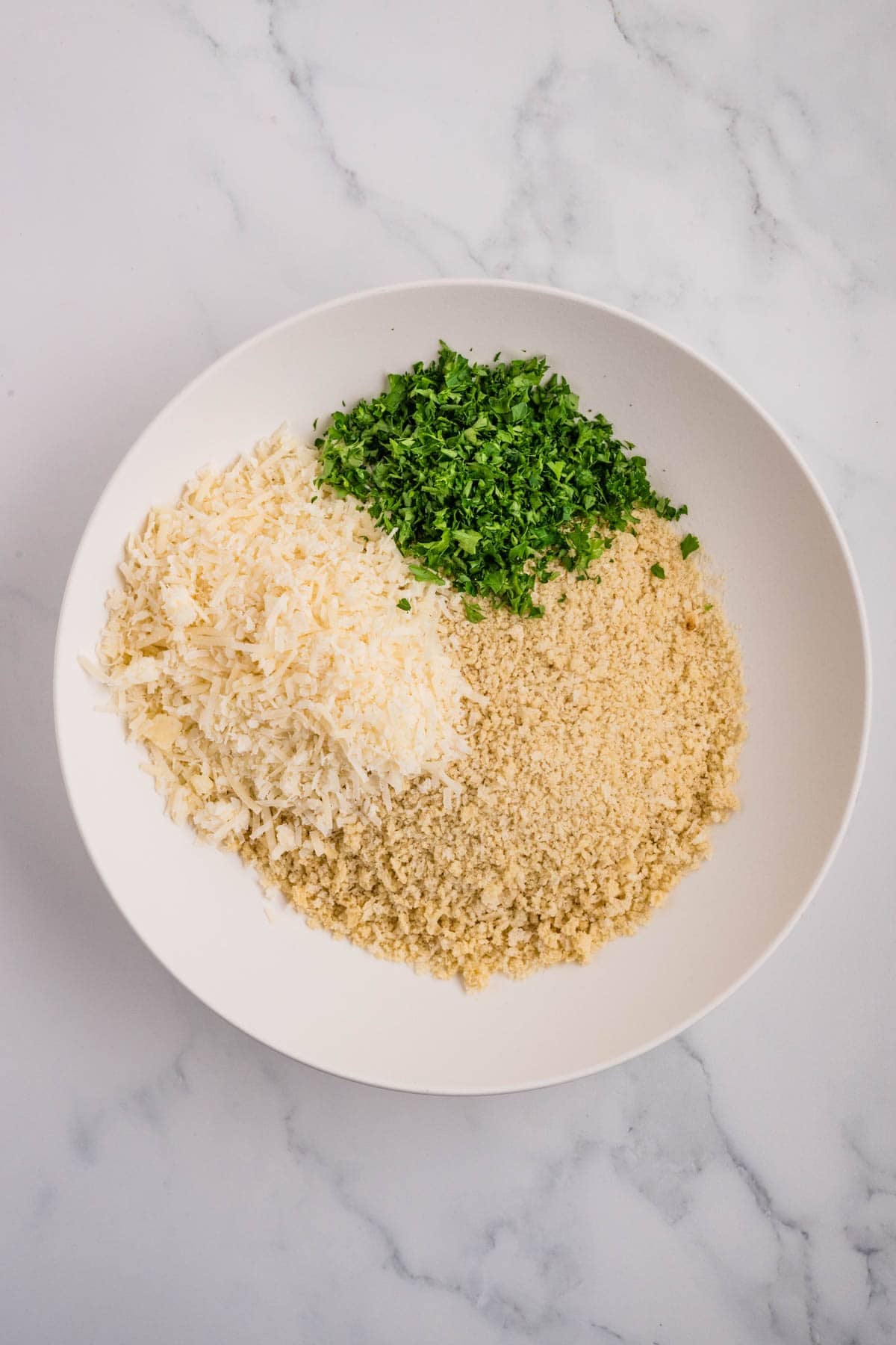 A dredging station of breadcrumbs, parmesan cheese, and parsley.