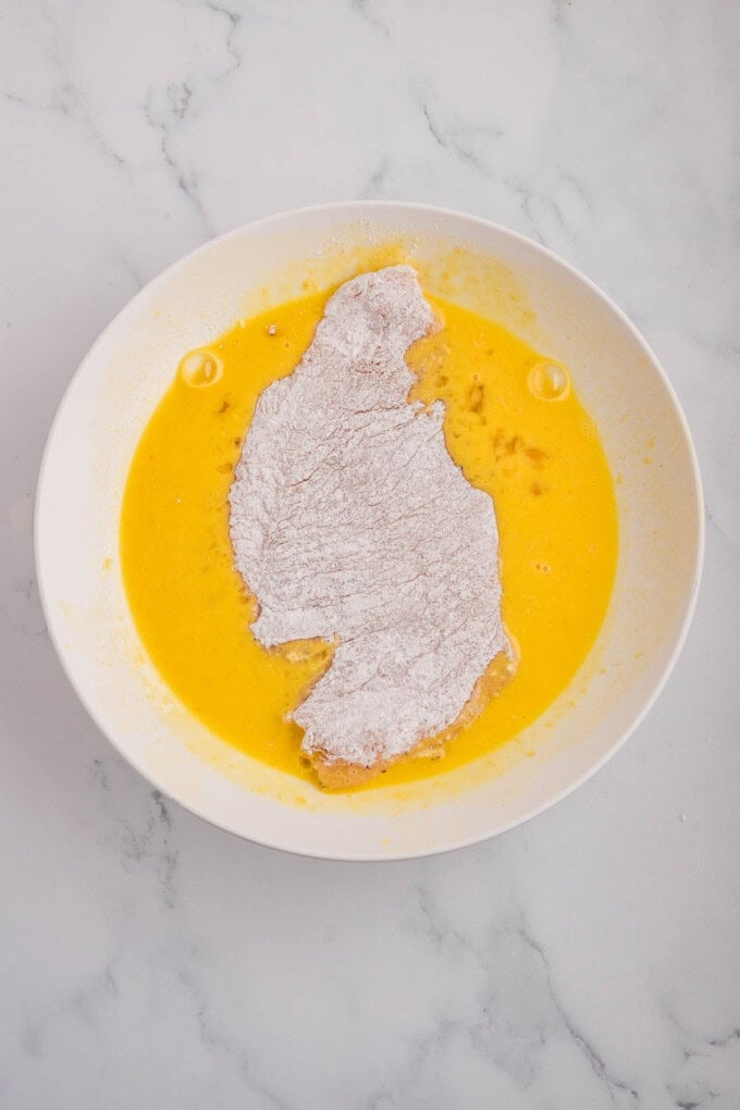 A chicken breast being dredged in egg wash.