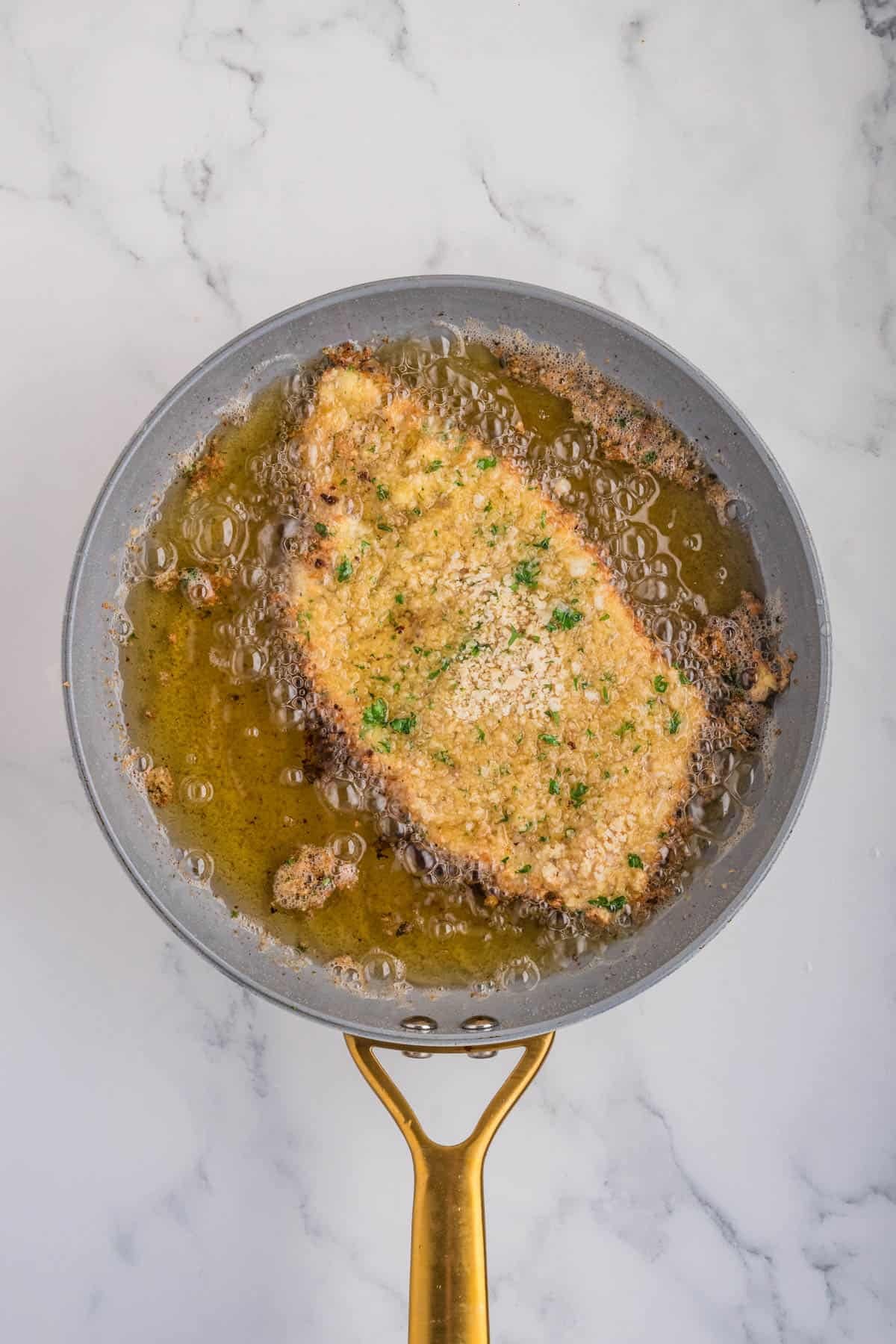 Breaded chicken milanese being fried in hot oil in a pan.