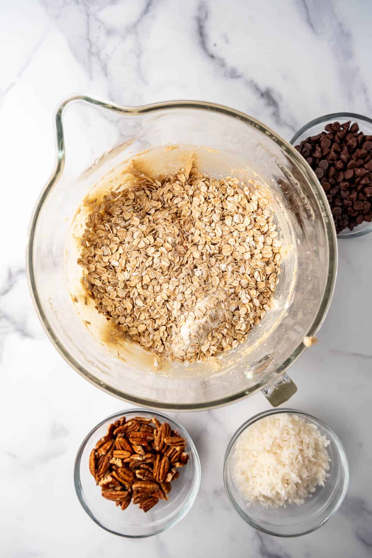 Oats and flour being added to cookie dough in a glass mixing bowl.