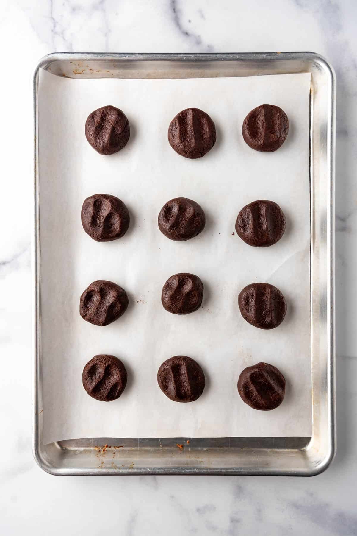 Mounds of chocolate cookie dough spaced apart on a baking sheet lined with parchment paper.