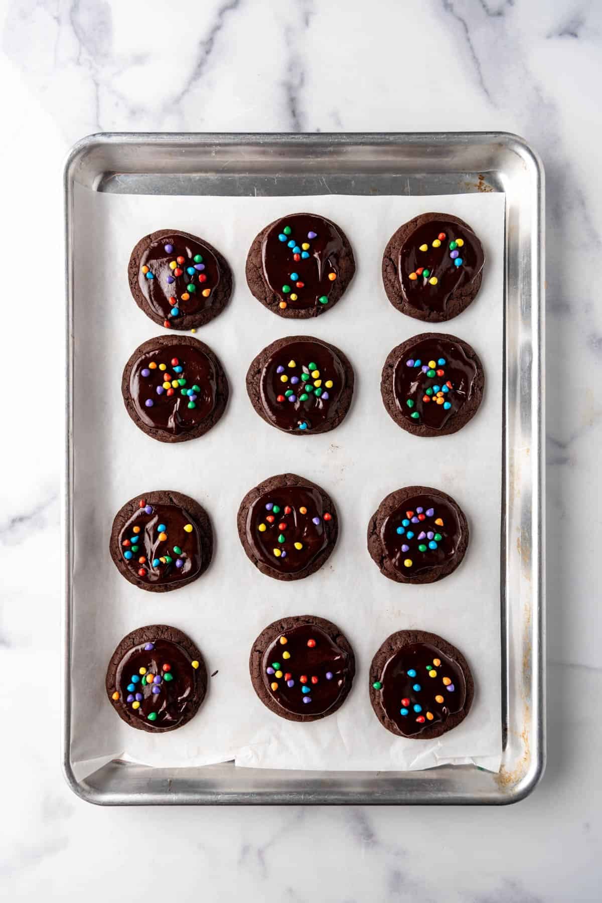 An overhead image of cosmic brownie cookies topped with chocolate ganache and rainbow chocolate candies.