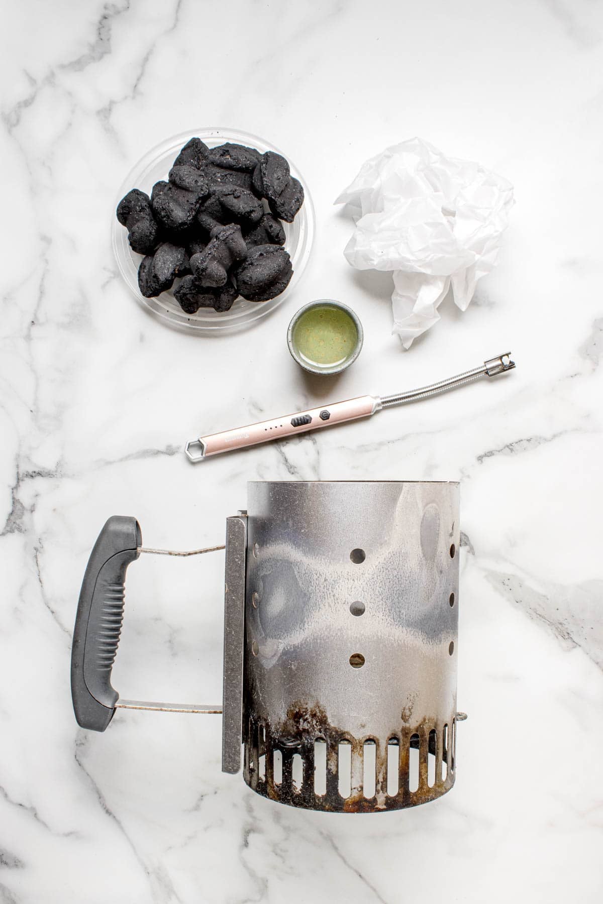 An overhead image of a chimney starter, charcoal briquettes, crumbled paper, and a lighter.