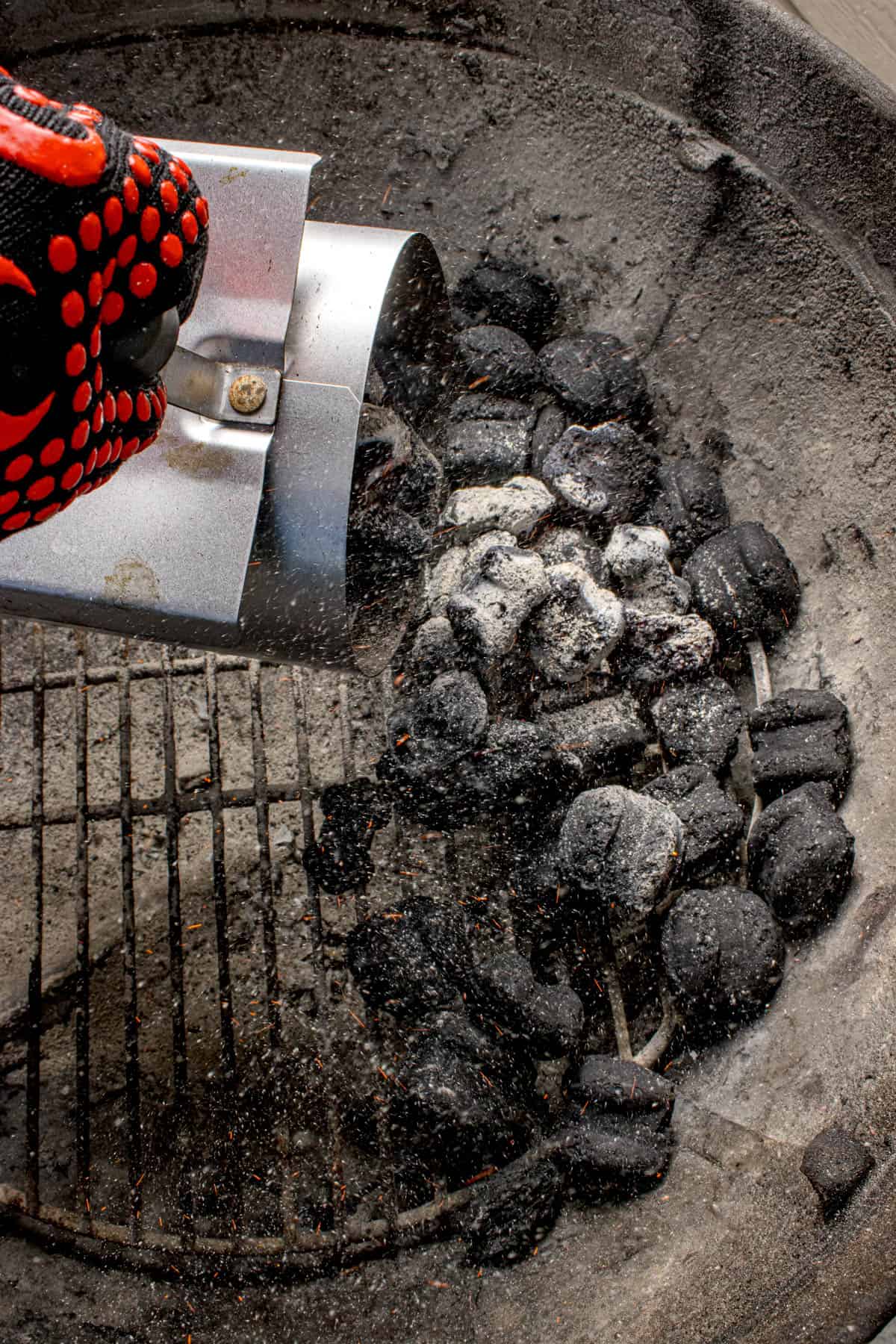 Lit charcoal briquettes being dumped into a grill.