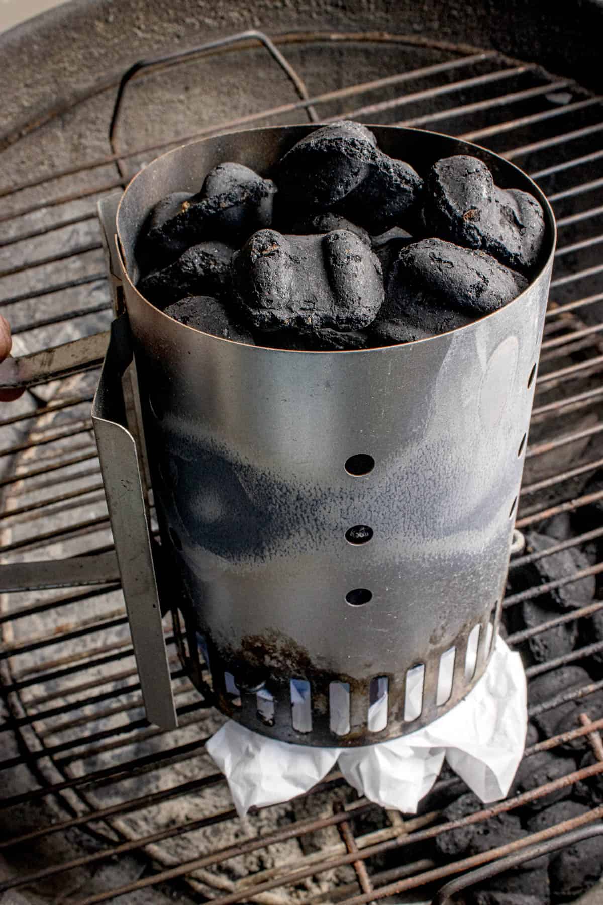 Adding charcoal to a chimney starter with paper underneath.