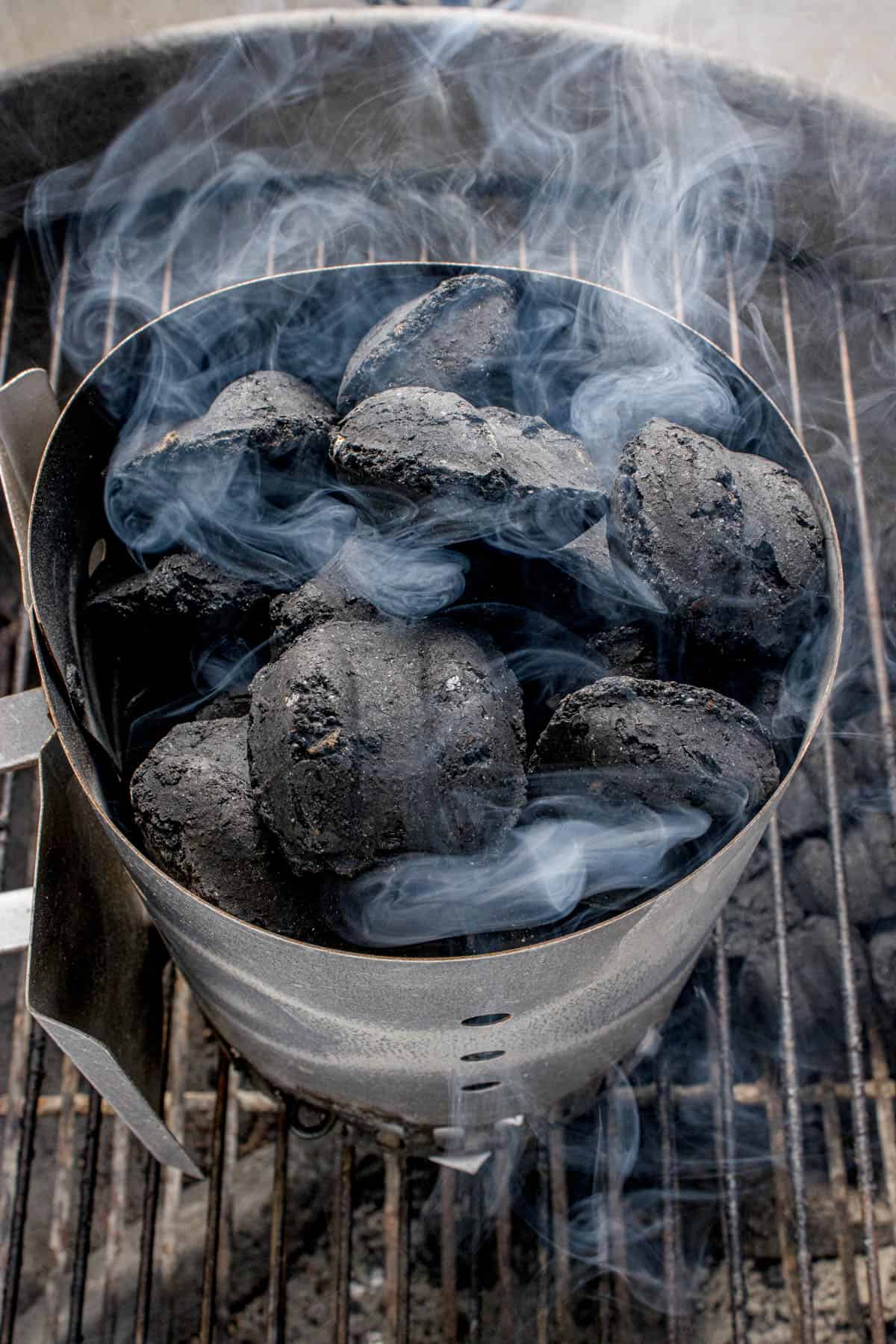 Smoke starting to rise off charcoal briquettes in a chimney starter.