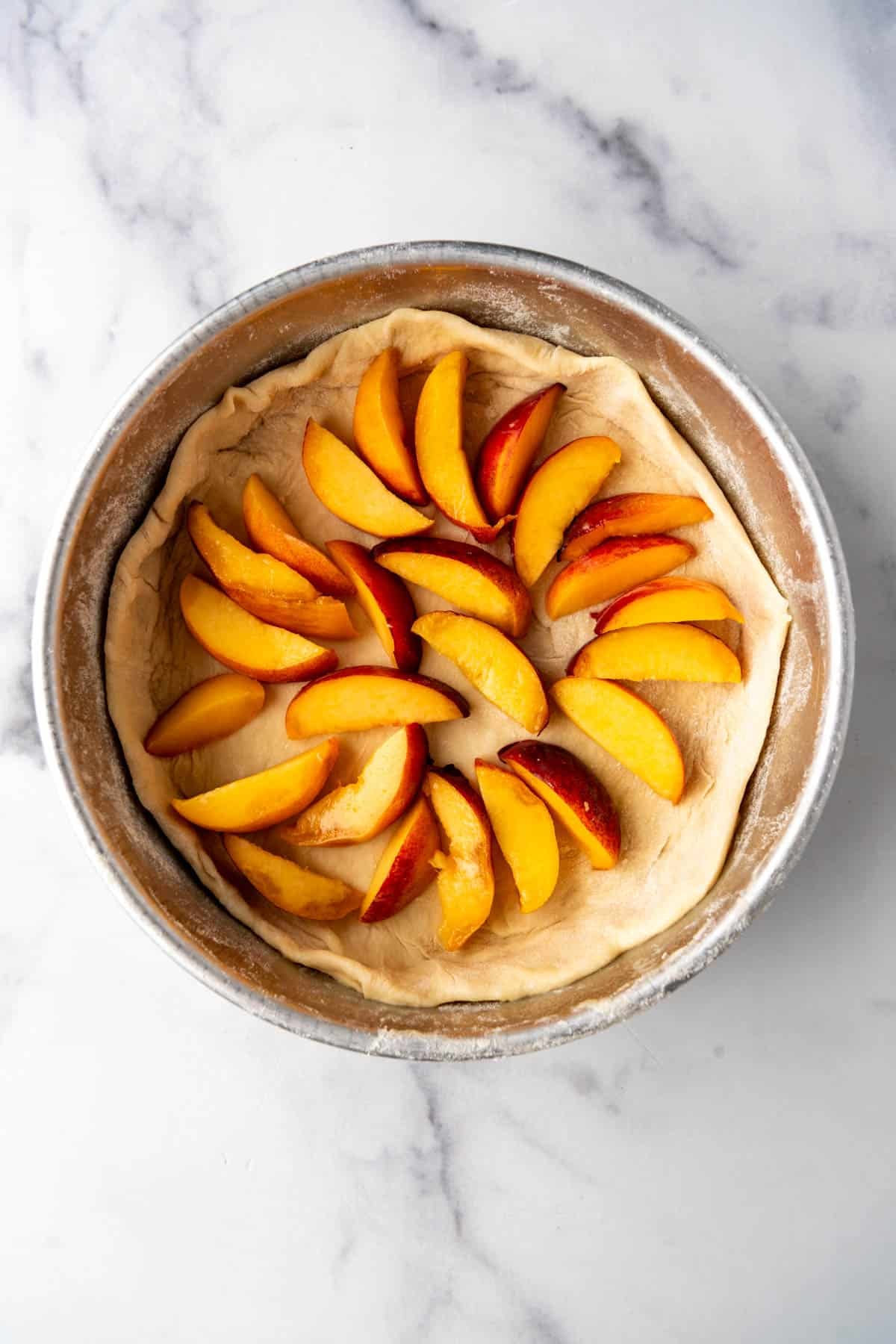 An overhead image of sliced peaches in a yeast dough crust in a pan.