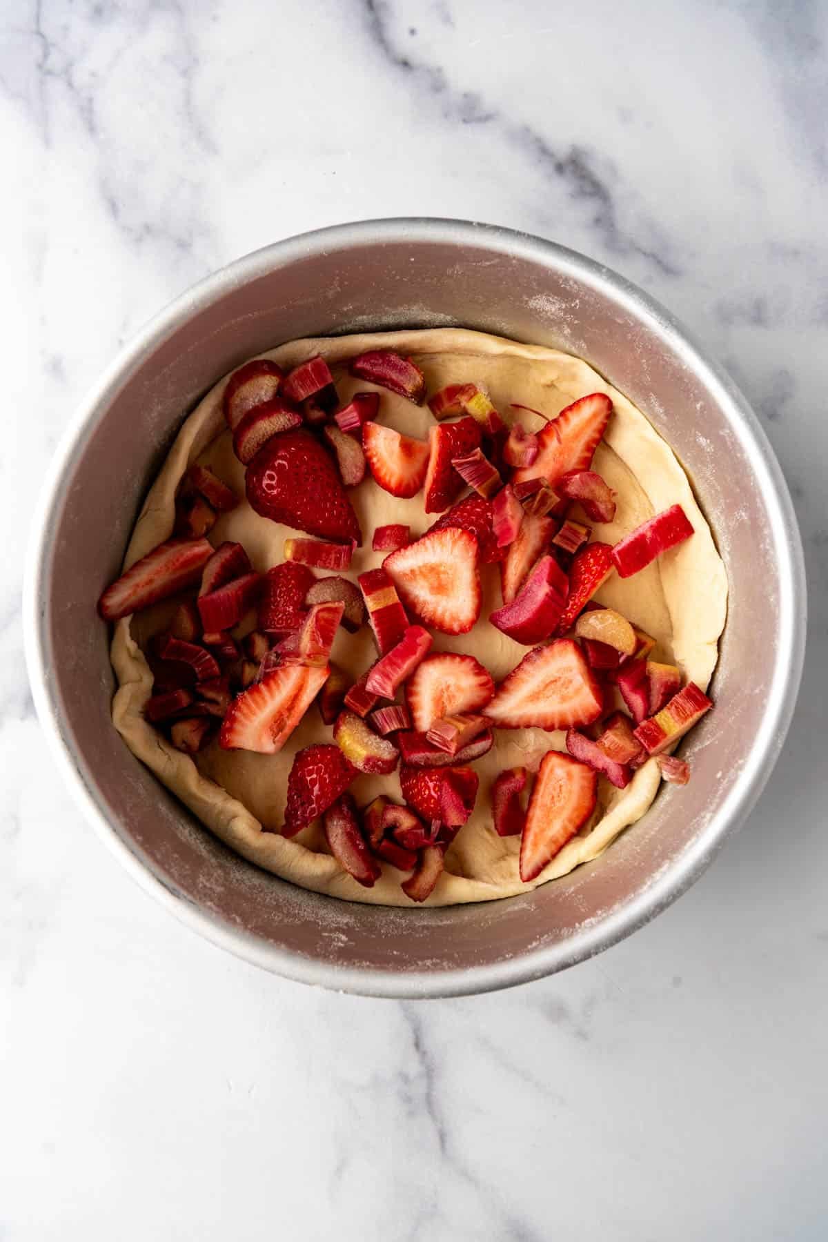 An overhead image of sliced strawberries and rhubarb in a yeast dough crust in a pan.