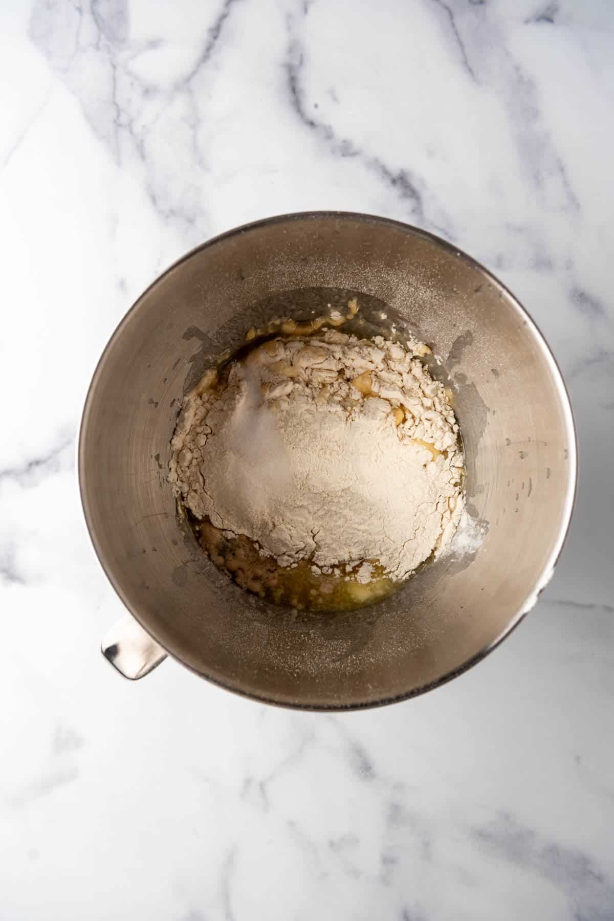 An overhead image of flour, warm water, yeast, sugar, salt, eggs, and butter in a mixing bowl.