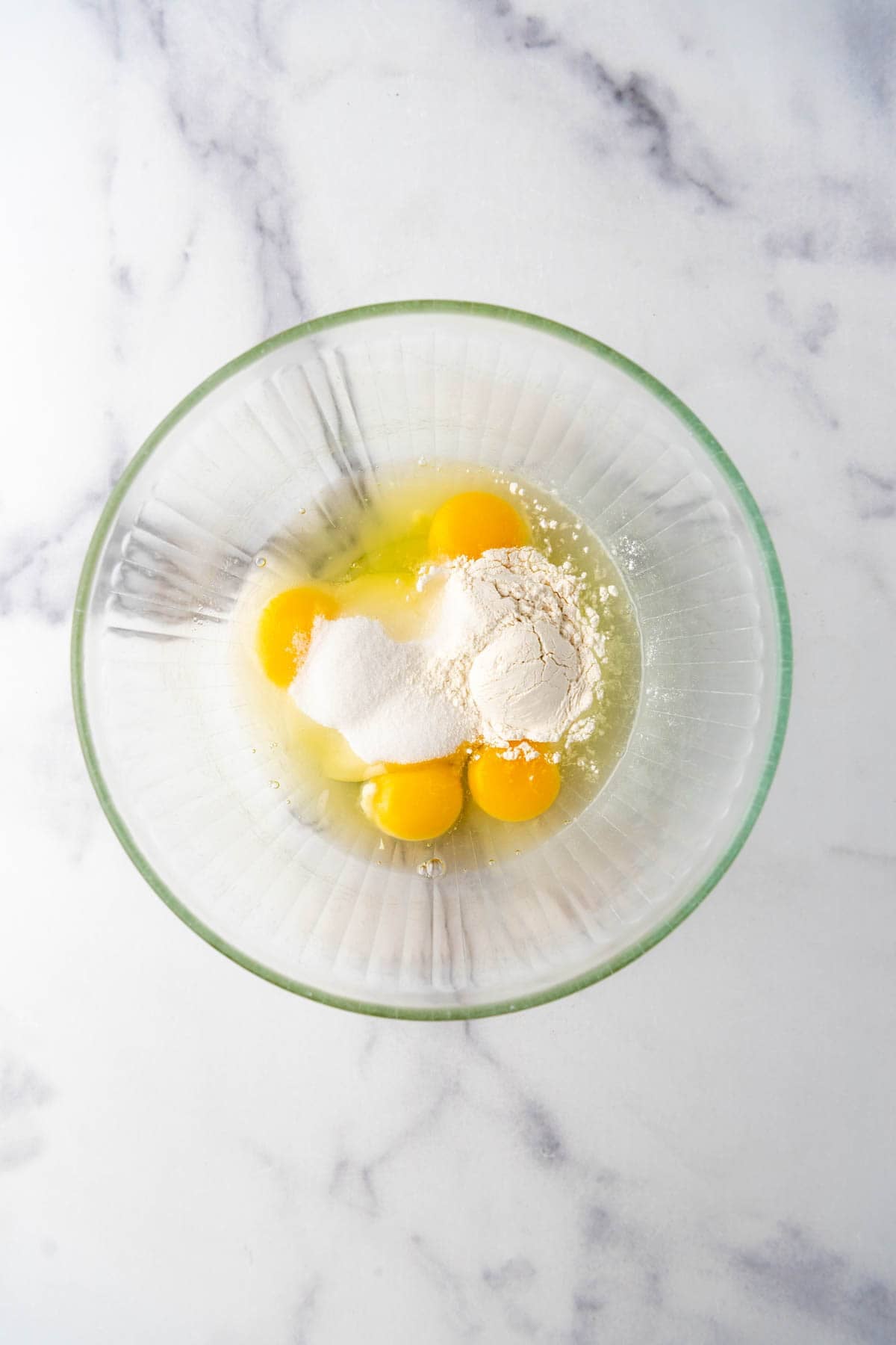 Flour, sugar, and eggs being combined in a glass mixing bowl.