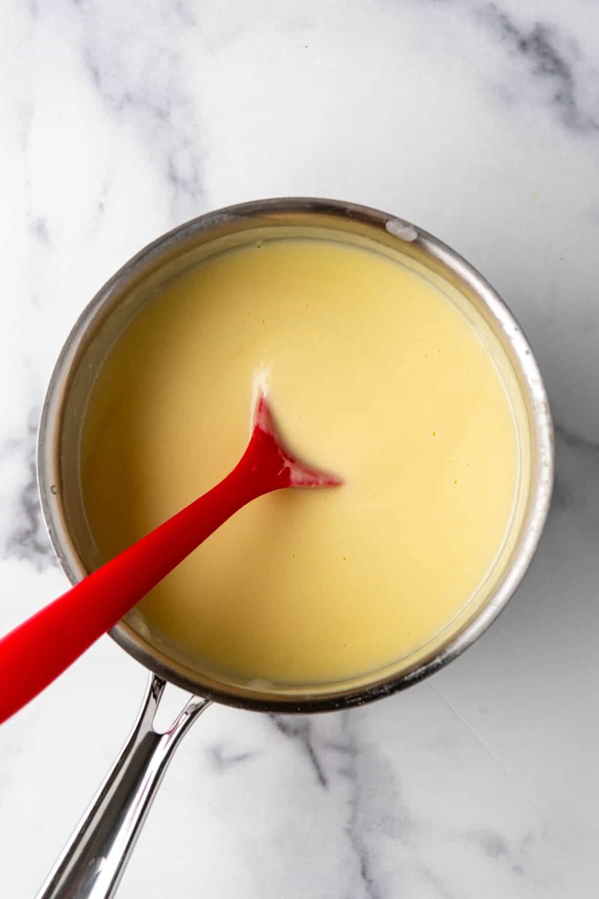 Custard in a saucepan with a red silcone spoon.