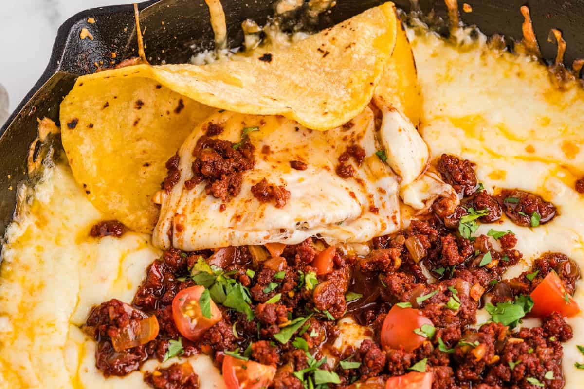 A side view of a warm tortilla in melted cheese and chorizo in a skillet.