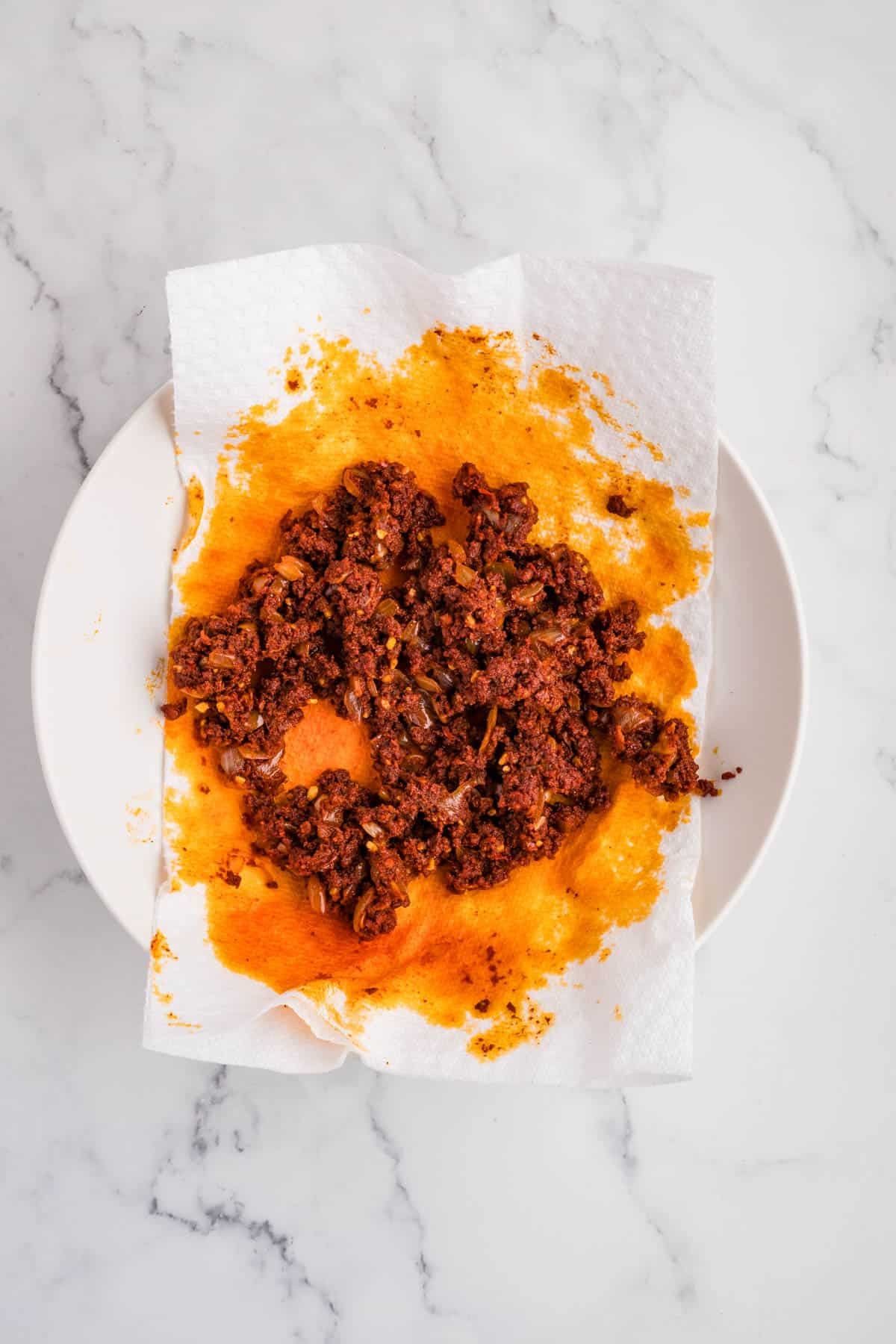 Crumbled cooked chorizo on a paper towel lined plate.
