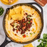 An overhead image of a skillet of queso fundido next to tortilla chips, cilantro, and shredded cheese.