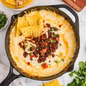 An overhead image of a skillet of queso fundido next to tortilla chips, cilantro, and shredded cheese.