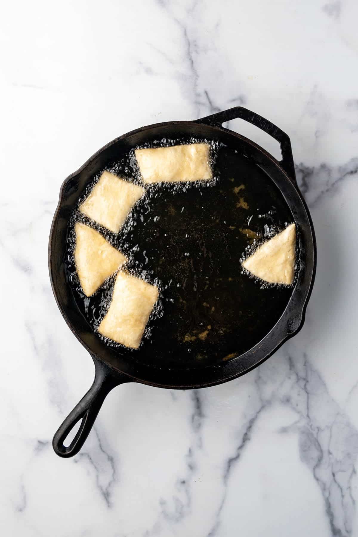 Sopapillas being fried in hot oil in a large skillet.