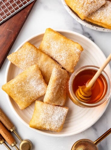 An overhead image of a plate of sopapillas next to a jar of honey.