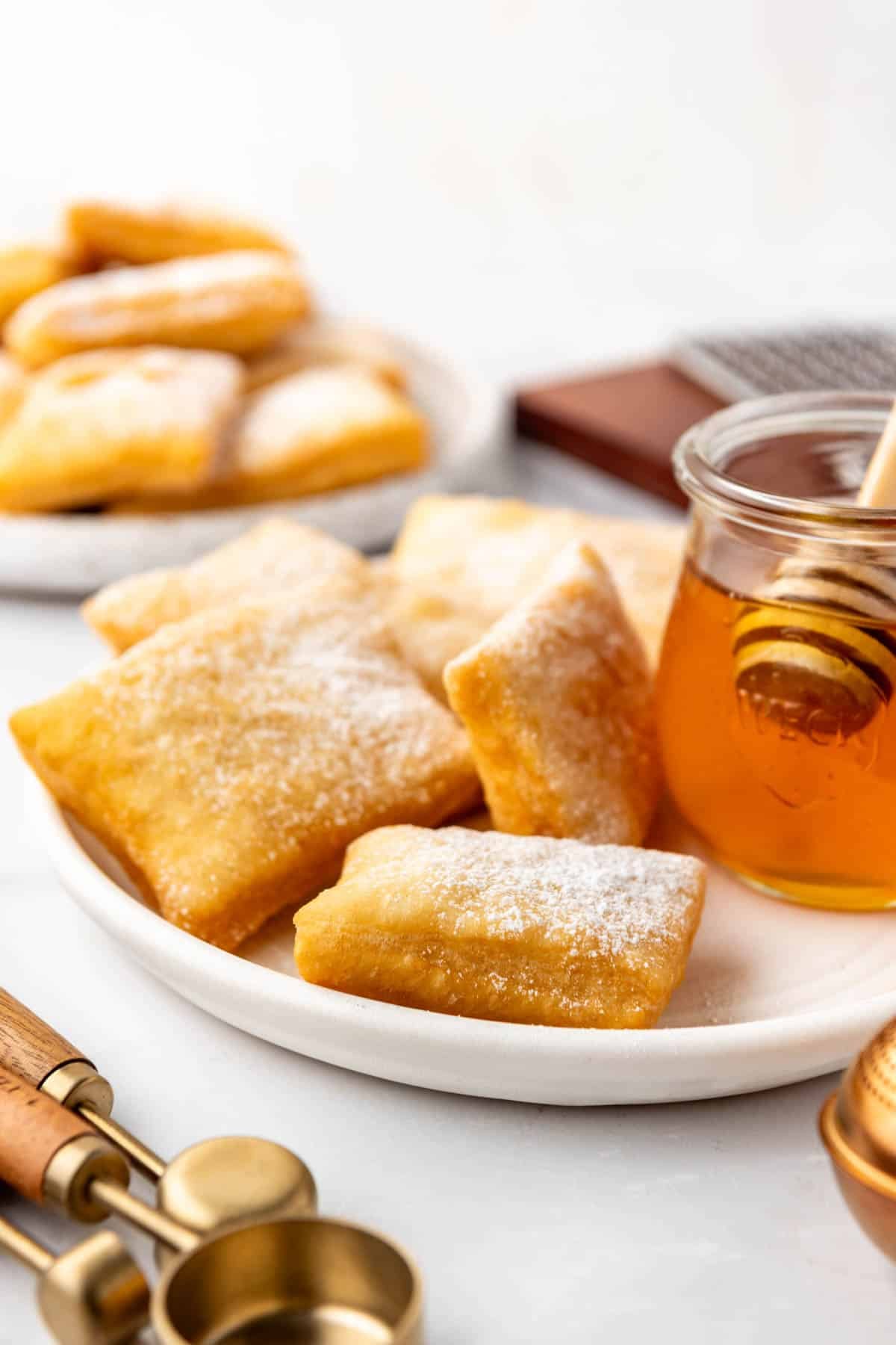 Warm sopapillas on a white plate next to a jar of honey.
