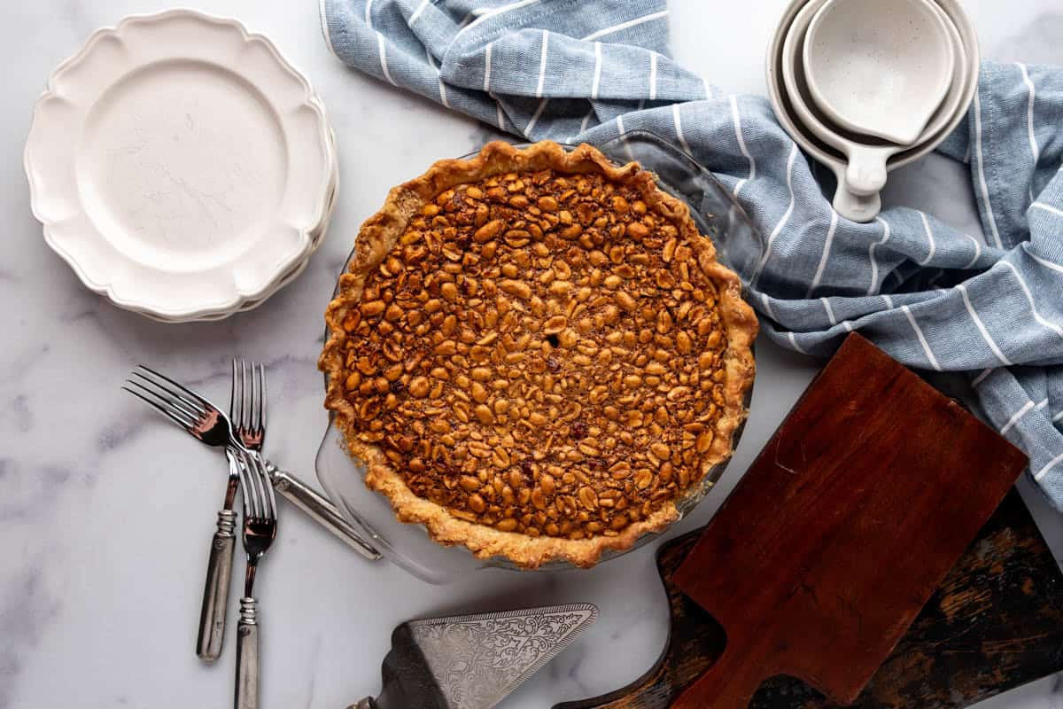 An overhead image of a baked Virginia peanut pie surrounded by plates and a blue cloth napkin.