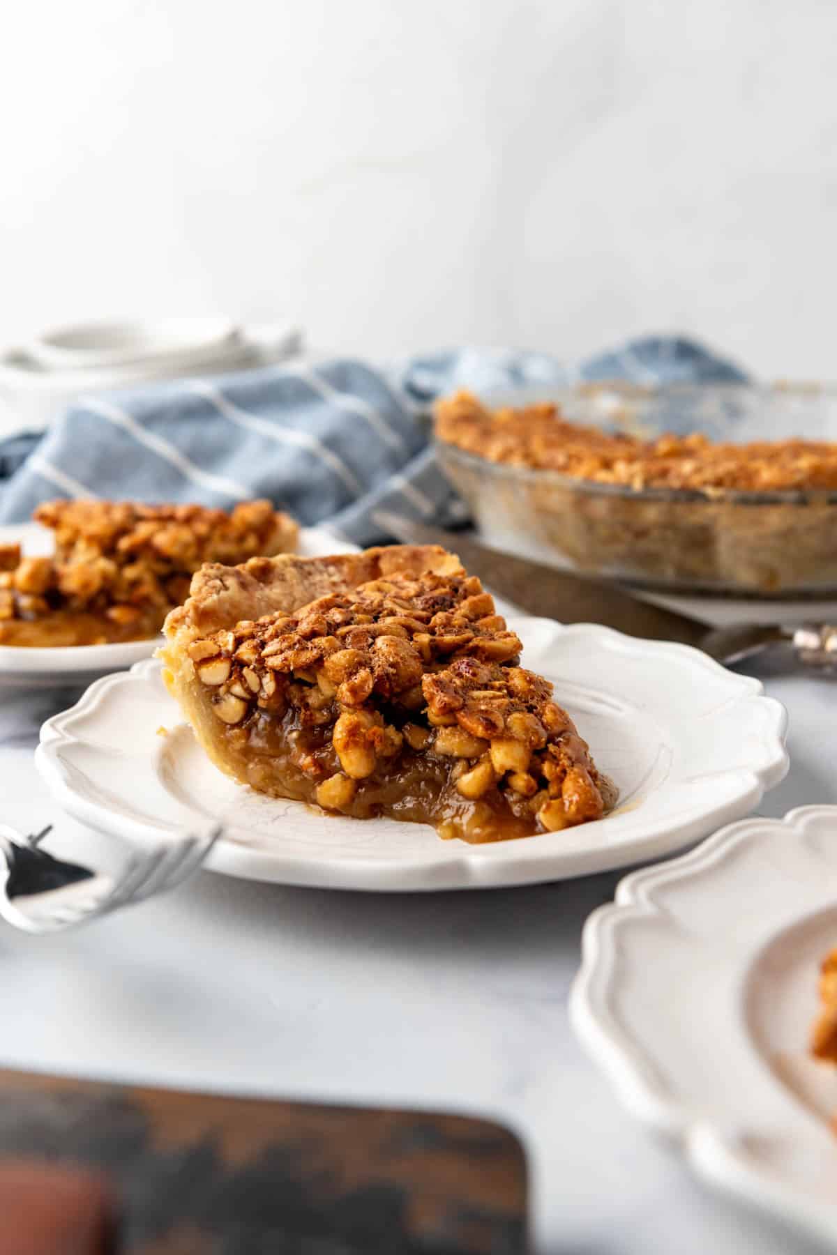 A slice of gooey peanut pie on a plate with more pie in the background.