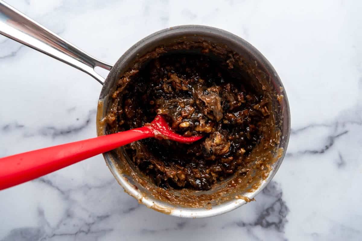 An overhead image of the filling for an Alabama Lane Cake in a saucepan with a red silicone spoon.