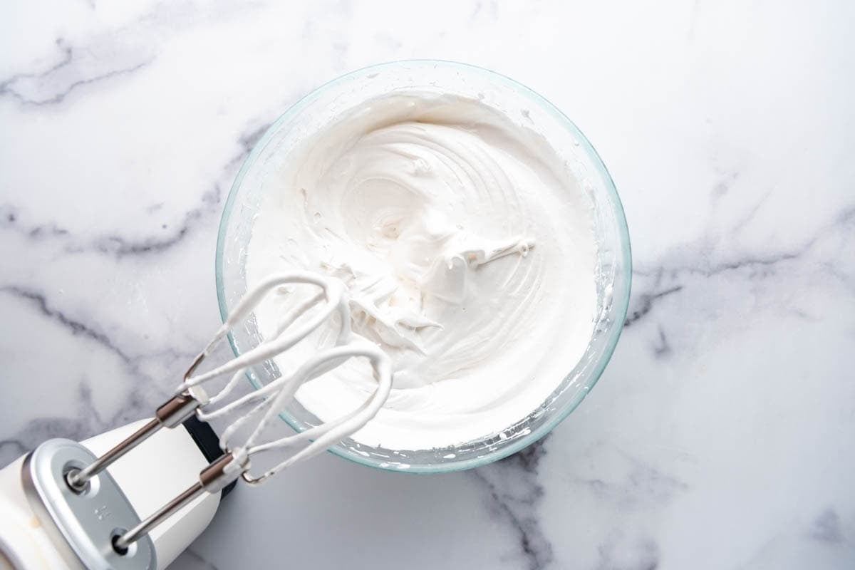 A finished batch of 7-minute frosting in a glass mixing bowl with an electric mixer.