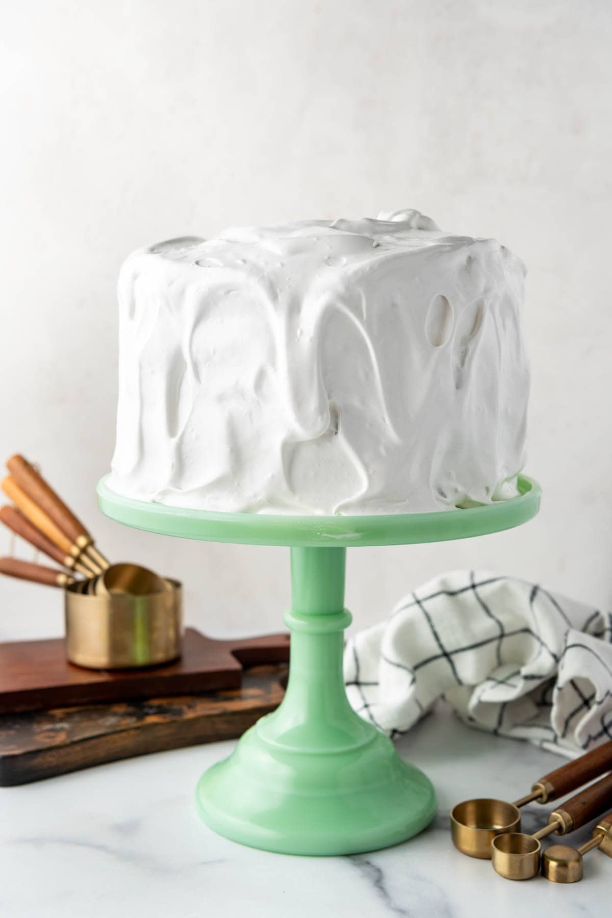 An image of a Lane Cake frosted with 7-minute frosting on a light green cake stand.