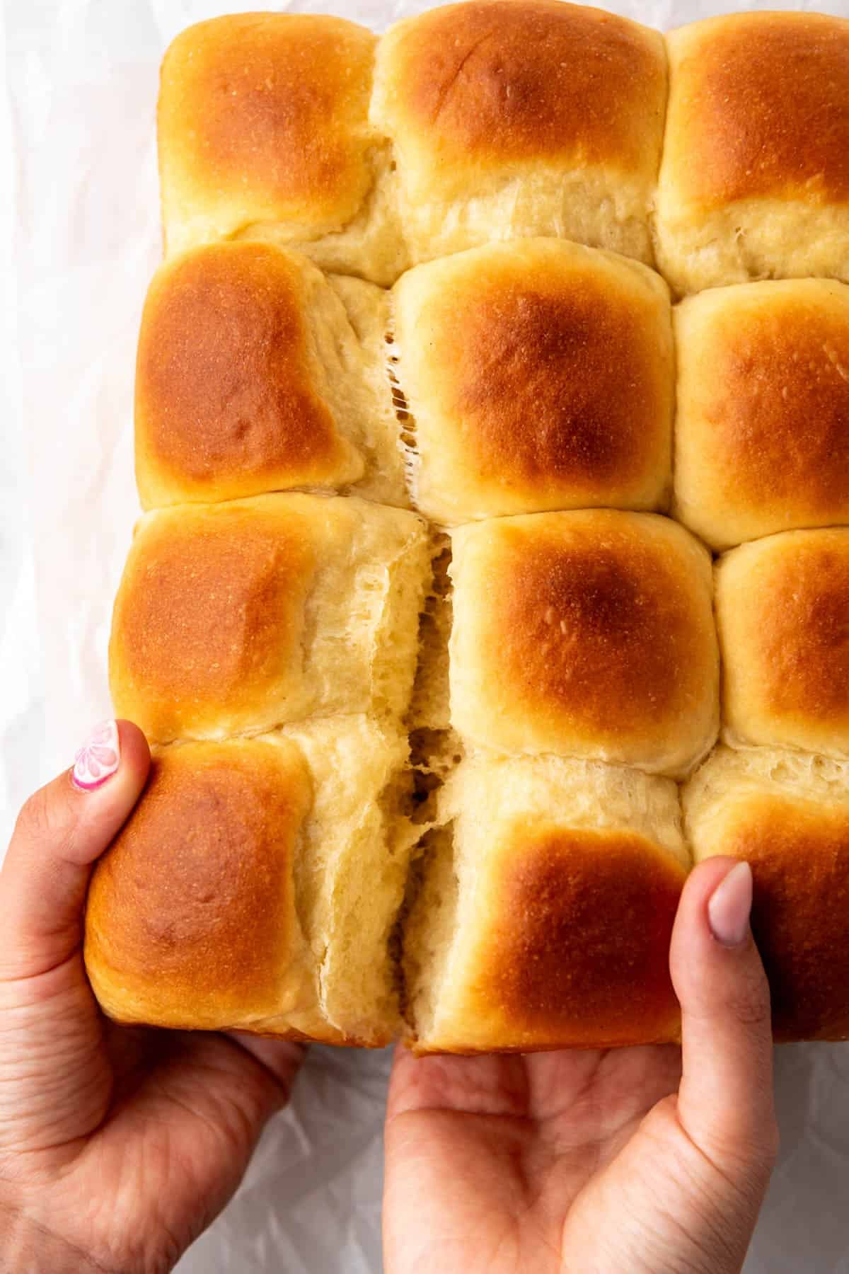 Hands separating soft homemade Hawaiian rolls.