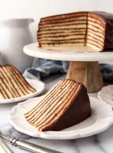 Slices of chocolate Smith Island cake on plates in front of the rest of the sliced cake on a cake stand.