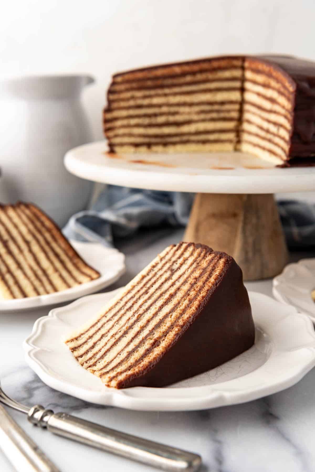 Slices of chocolate Smith Island cake on plates in front of the rest of the sliced cake on a cake stand.