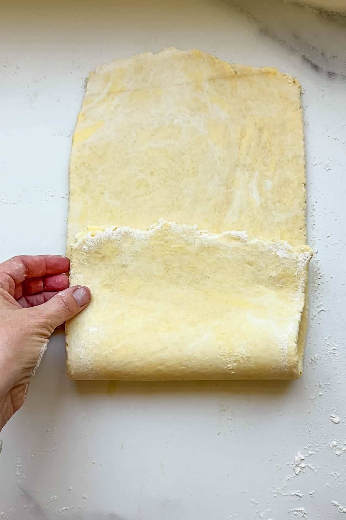 A hand folding dough onto itself to create laminated layers.
