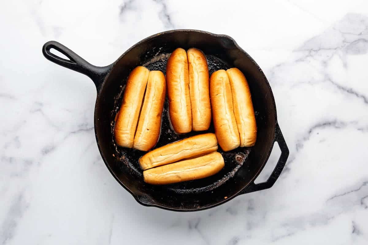 Hot dogs buns being toasted in a large skillet.