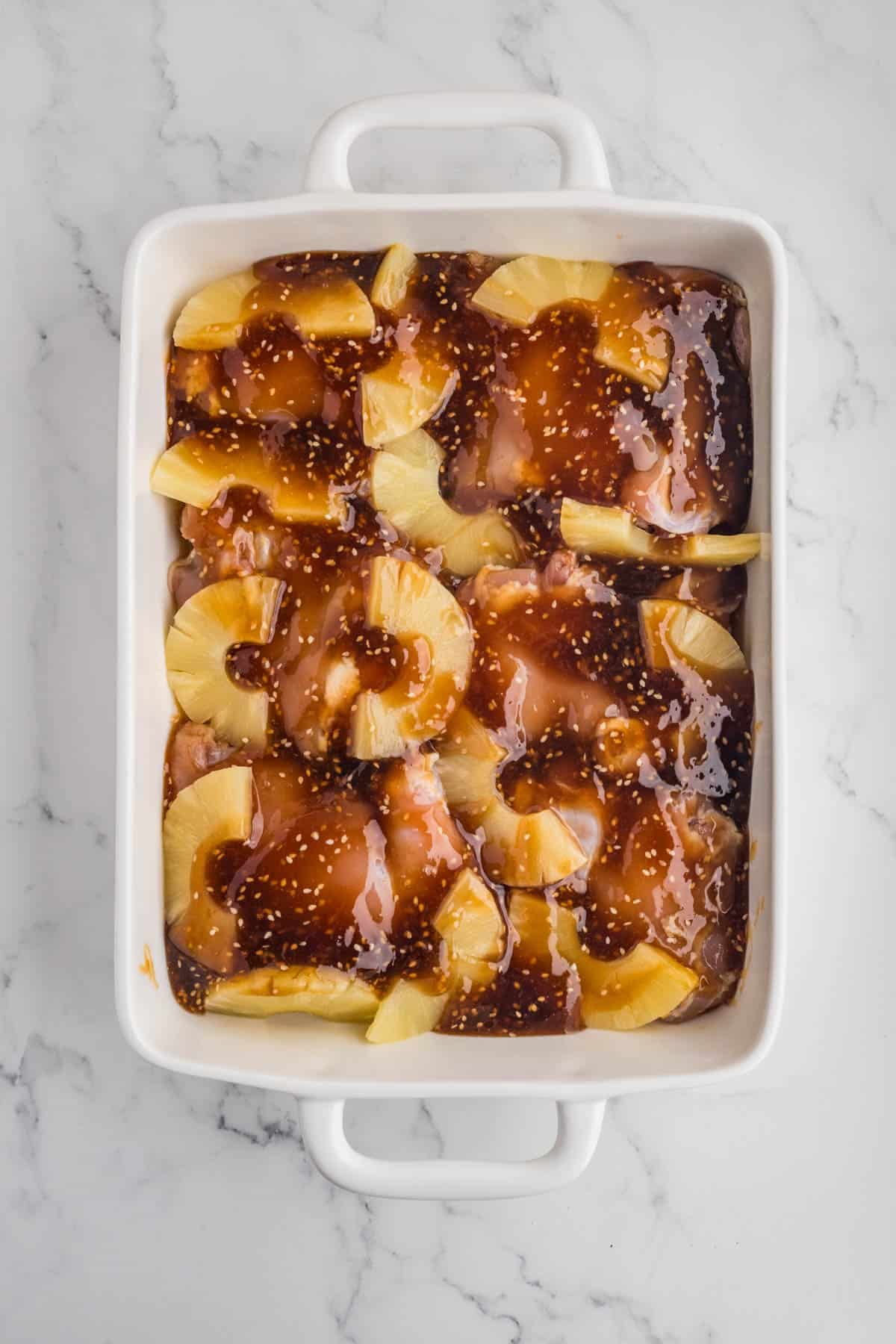 Chicken and pineapple in a large baking dish with homemade teriyaki sauce poured over the top.