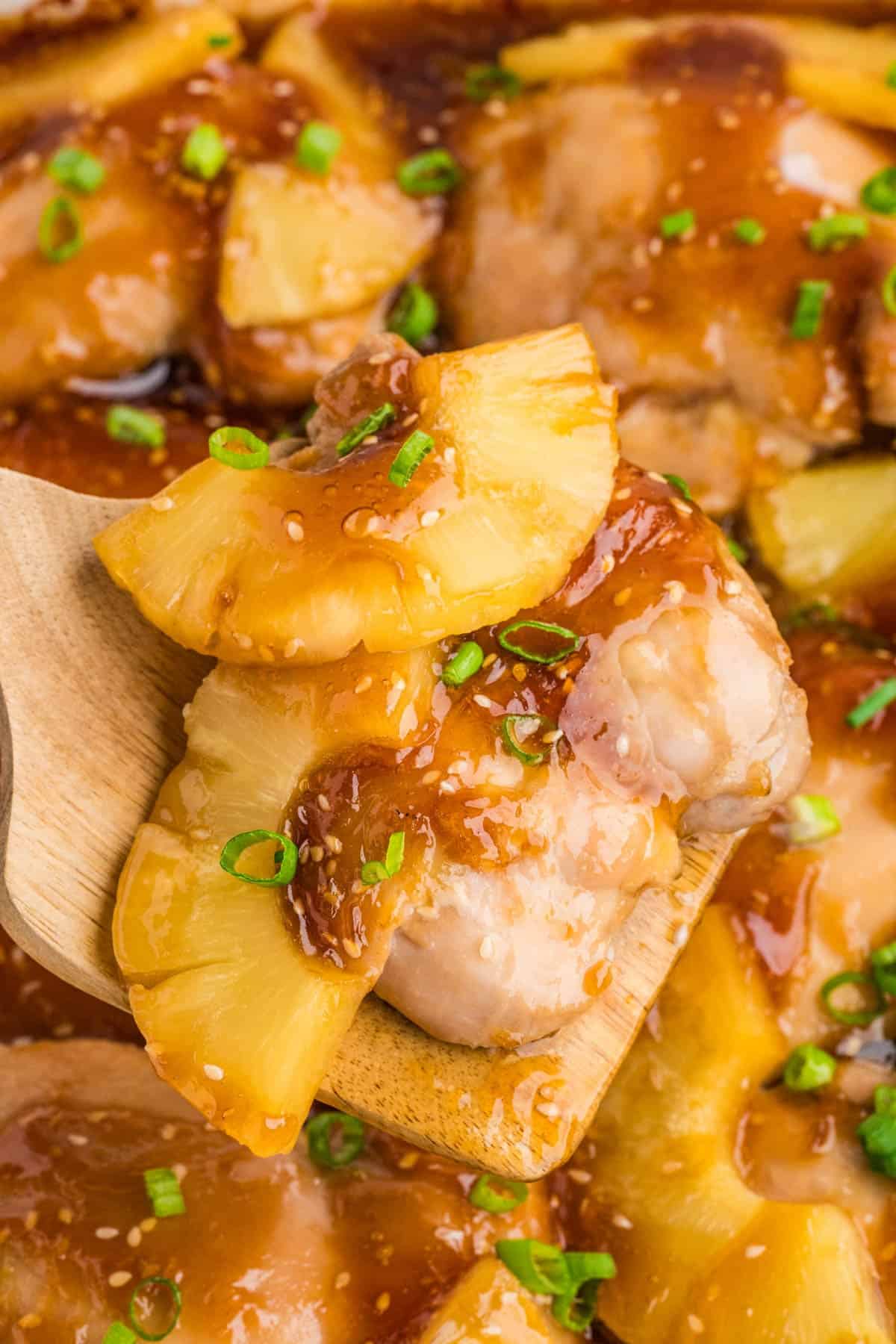 A close up image of a chicken thigh in teriyaki sauce with pineapple slices.