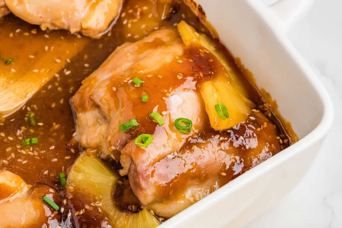 Baked chicken thighs in teriyaki sauce with pineapple slices in a white casserole dish.