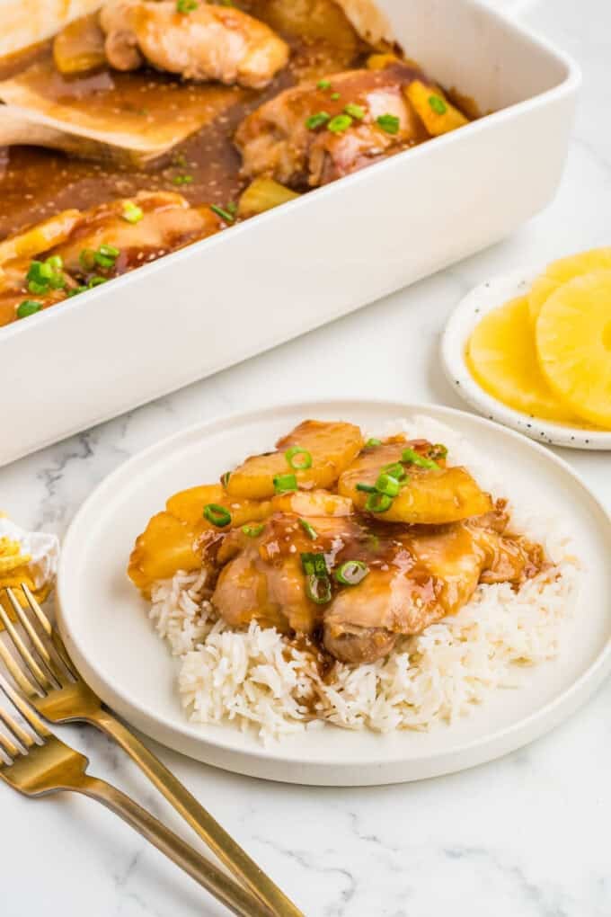 Baked pineapple teriyaki chicken on a plate of rice with forks next to it.