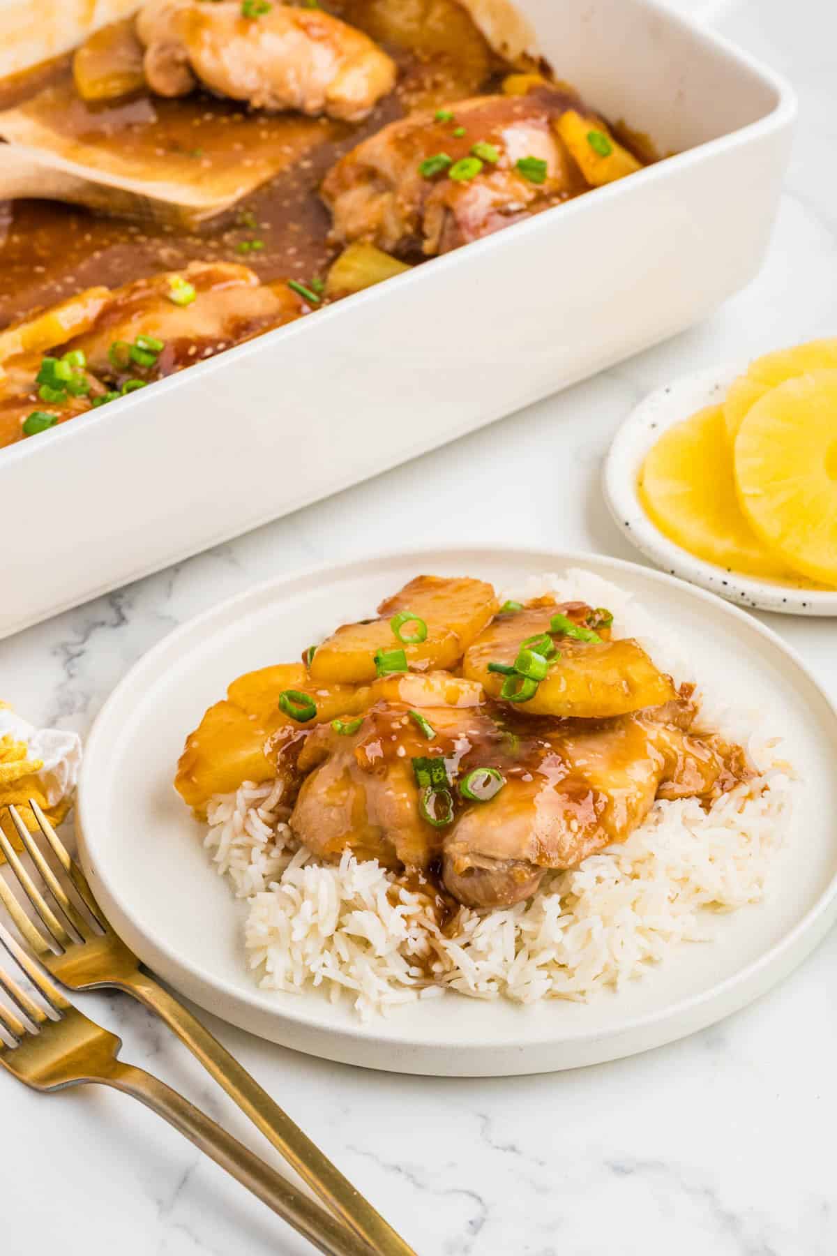 Baked pineapple teriyaki chicken on a plate of rice with forks next to it.