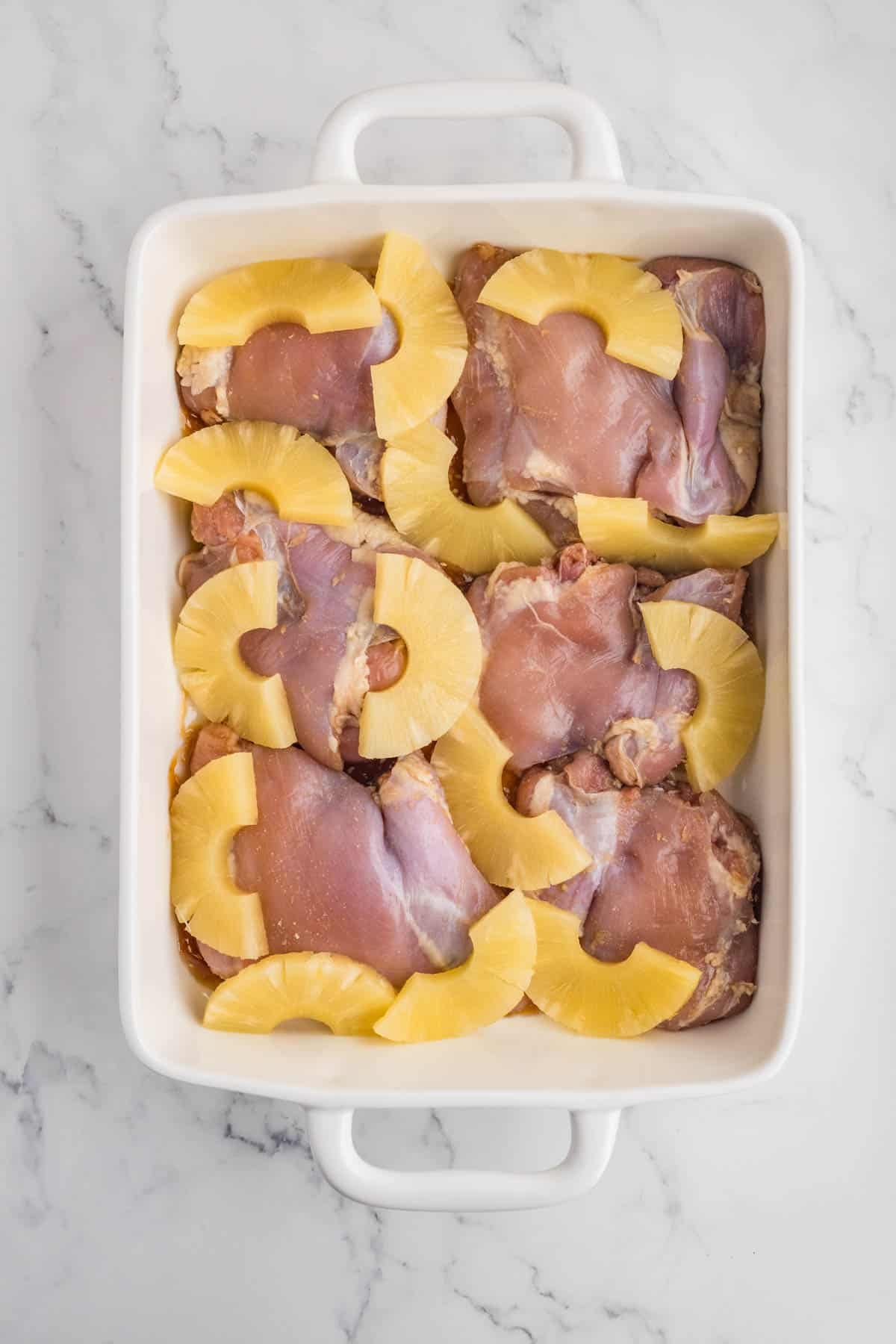 Chicken thighs with pineapple slices in a baking dish.