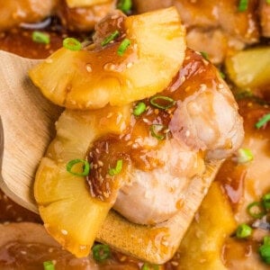 A wooden spoon holding baked teriyaki pineapple chicken.