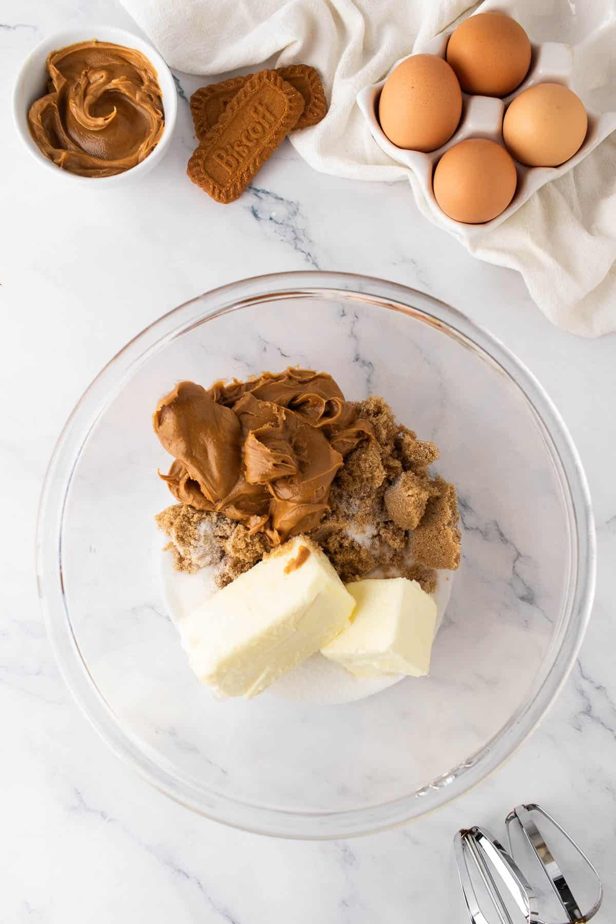 Combining butter, cookie butter, and sugar in a mixing bowl with eggs nearby.