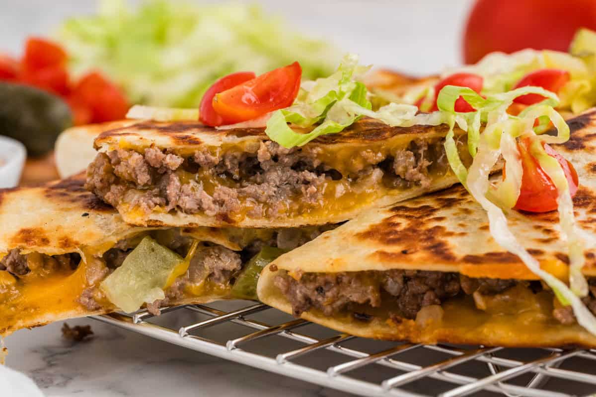 Stacked cheeseburger quesadillas filled with ground beef and cheese, then topped with burger toppings.